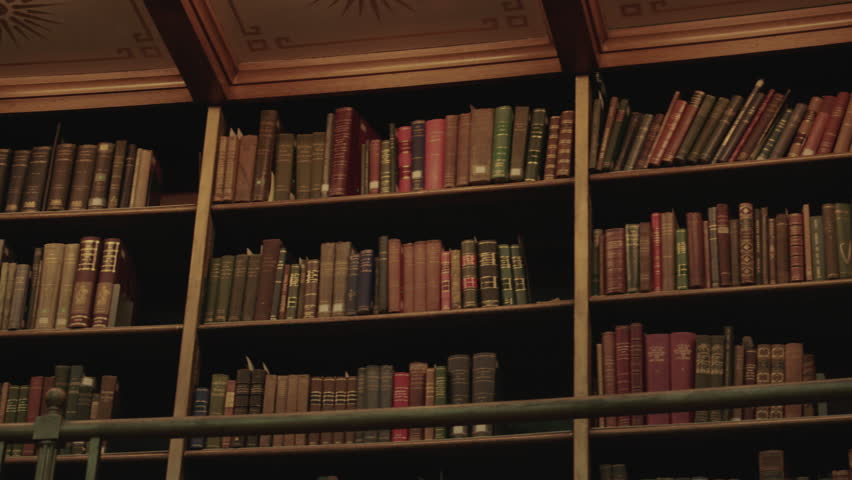 Close-up of classic wooden bookshelves filled with aged, colorful leather-bound books under warm light, capturing the timeless charm of a historic library interior.