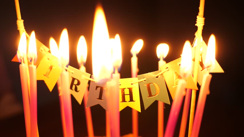 Happy birthday decoration on a cake with burning candles on dark background