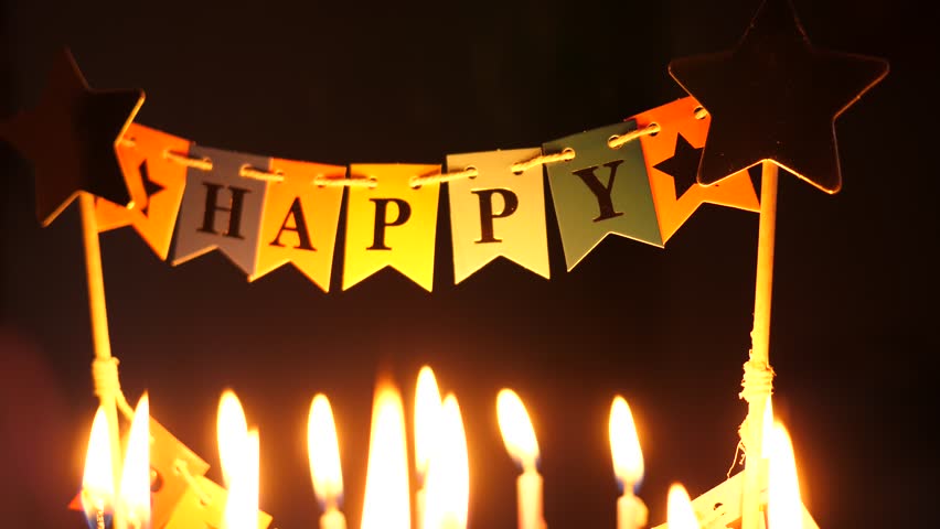 Happy birthday decoration on a cake with burning candles on dark background