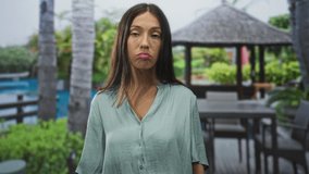 Woman pouting lips with closed eyes at hotel pool, wearing loose blouse by cabana; quiet disappointment. - Powered by Shutterstock - Get 15% off with code: PIKWIZARD15