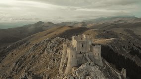 Cinematic drone shot of the ancient fortress of Rocca Calascio surrounded by the mountains of Abruzzo, Italy. Scenic hiking trail leading to the medieval castle on a rocky ridge at sunset. - Powered by Shutterstock - Get 15% off with code: PIKWIZARD15