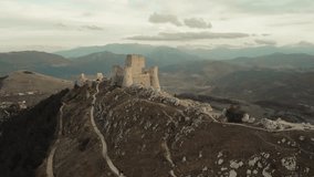 Cinematic drone shot of the ancient fortress of Rocca Calascio surrounded by the mountains of Abruzzo, Italy. Scenic hiking trail leading to the medieval castle on a rocky ridge at sunset. - Powered by Shutterstock - Get 15% off with code: PIKWIZARD15