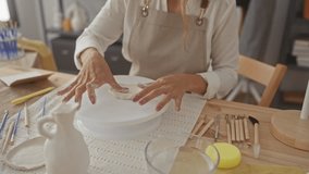 Young blonde woman wearing an apron kneading clay with bare hands on a wooden table in a studio; creativity focus artistry. - Powered by Shutterstock - Get 15% off with code: PIKWIZARD15