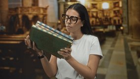 Woman holding ornate sacred books and adjusting glasses in a church building aisle, arms cradling volumes against her chest; contemplation. - Powered by Shutterstock - Get 15% off with code: PIKWIZARD15