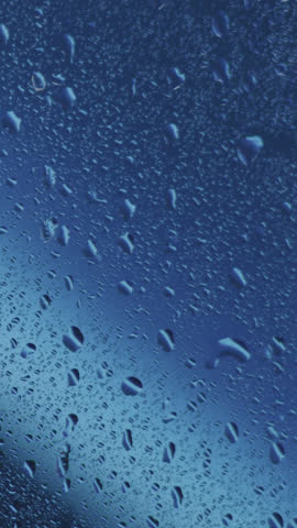 Rain-splattered windowpane with water droplets gently sliding in dim evening light, moody soft focus, ambient atmosphere, soothing scene, perfect for cinematic, introspective, melancholic visuals.