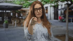 Woman with red hair in a striped shirt wearing eyeglasses tapping her temple and gazing ahead on a city street; introspection. - Powered by Shutterstock - Get 15% off with code: PIKWIZARD15