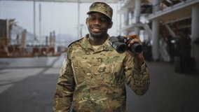 Soldier man holding binoculars near shoulder, smiling in an airport terminal; pride duty vigilance service. - Powered by Shutterstock - Get 15% off with code: PIKWIZARD15