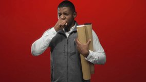 Man coughing into fist holding rolled architectural blueprints while wearing white shirt and gray vest in a red studio; sick concern. - Powered by Shutterstock - Get 15% off with code: PIKWIZARD15