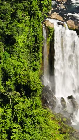 Two- tiered waterfall in mountain forest with rainbow. Limunsudan Falls. Mindanao, Philippines. Vertical, stories.