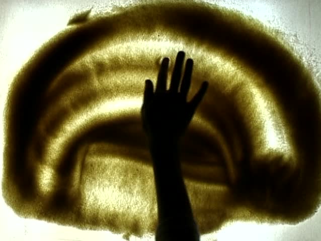 The hand draws a car silhouette on a sandy surface  