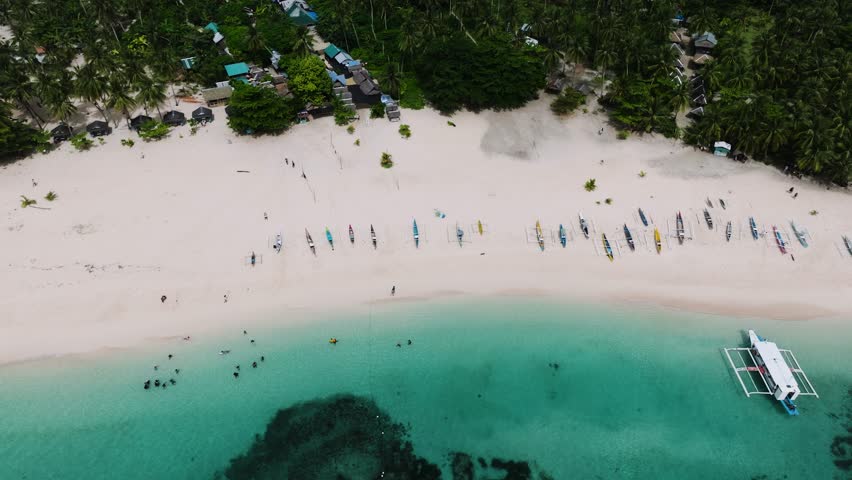 Top view of traditional boats rest on the white sandy beach near turquoise waters. Daku Island. Siargao, Philippines.