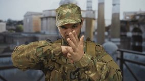 Young hispanic man in camouflage uniform blocks a punch with raised hand at building ruins; determination. - Powered by Shutterstock - Get 15% off with code: PIKWIZARD15