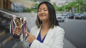 Young woman triumphantly holding trophy cup on city street showcasing success and achievement outdoors with smiling expression and modern urban backdrop. - Powered by Shutterstock - Get 15% off with code: PIKWIZARD15