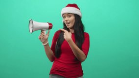 Woman in santa hat pointing finger at megaphone in studio, red top and exposed hand gesture for announcement; joyful holiday spirit. - Powered by Shutterstock - Get 15% off with code: PIKWIZARD15