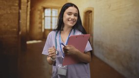 Woman nurse smiling while holding a pink clipboard in a hospital building hallway near a window; compassion care hope. - Powered by Shutterstock - Get 15% off with code: PIKWIZARD15