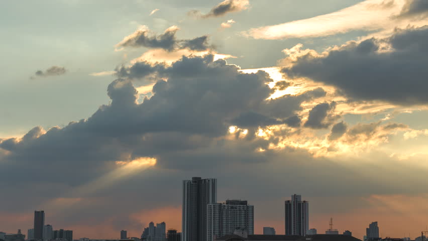 Time-lapse of Warm beams breaking through the clouds, illuminating the city with a divine glow.