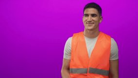 Man engineer in orange safety vest points finger in purple studio while smiling and indicating direction; confidence guidance safety. - Powered by Shutterstock - Get 15% off with code: PIKWIZARD15