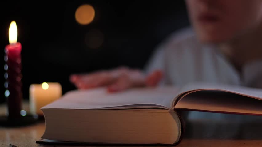 Close-up of a man reading an old book or Bible in the dark with dramatic lighting, conveying faith, history, knowledge, and thoughtful quiet moments.