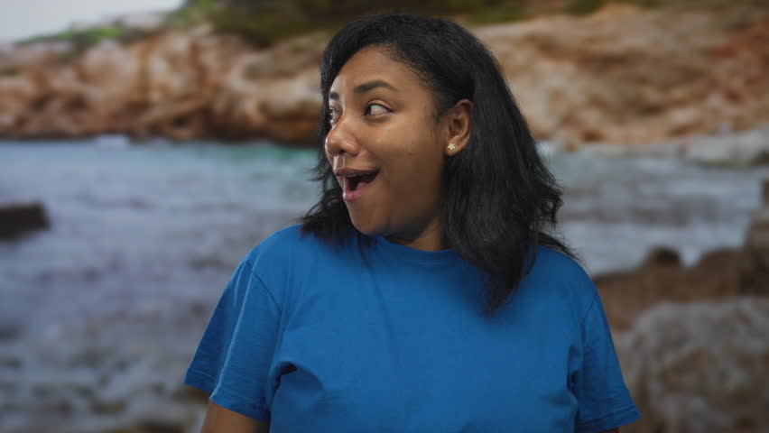 Woman in blue shirt shows bare arms and smiles while turning head toward camera in studio; joy optimism.