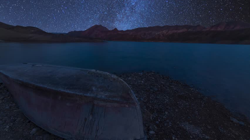 Small lake and mountains with boat under milky way galaxy timelapse.