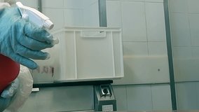 A worker in protective gear, including gloves, is using a spray bottle to apply disinfectant in an area that appears to be used for food preparation or production. - Powered by Shutterstock - Get 15% off with code: PIKWIZARD15