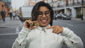 Woman smiling holding litecoin on city street giving thumbs-up representing cryptocurrency enthusiasm outdoors. - Powered by Shutterstock - Get 15% off with code: PIKWIZARD15
