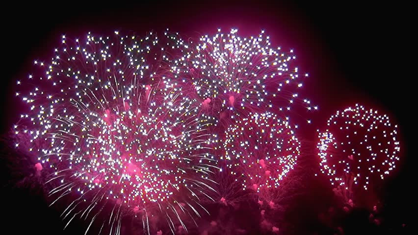 A beautiful spectacle of bursting pink and white fireworks lights up the night sky in a dazzling celebration of joy and festivity