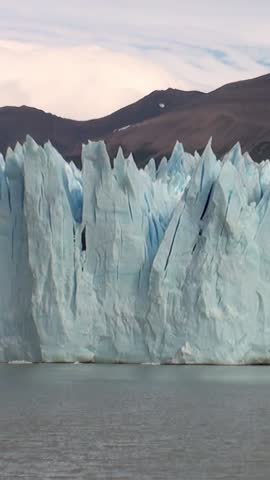 Experience breathtaking beauty of towering glaciers in Patagonia Andes. These icy giants reflect vibrant hues of landscape while their sheer faces loom above serene waters in Argentina.