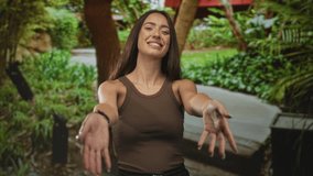 Woman reaching arms forward on a park path, smiling with open hands and sleeveless top; friendly greeting joy. - Powered by Shutterstock - Get 15% off with code: PIKWIZARD15