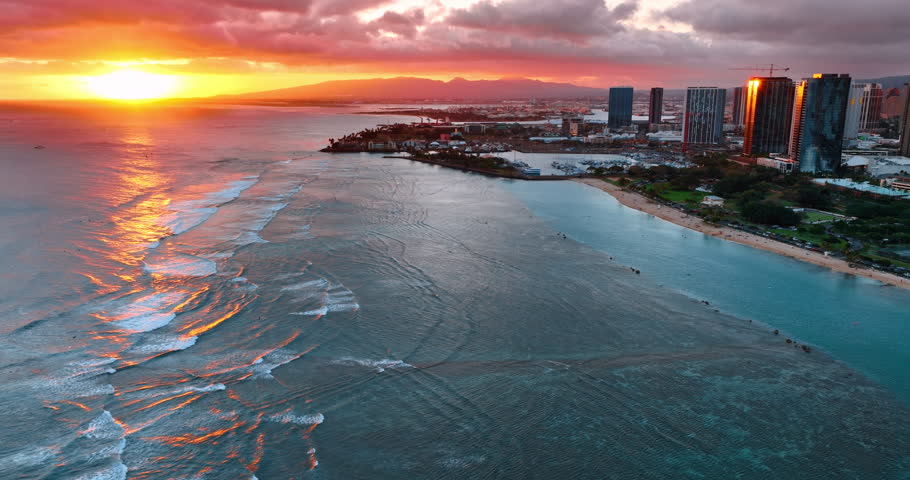 Bright sun and orange light in the sky at sunset. Drone flight over the waterscape of the Pacific Ocean at the shore of Honolulu, Hawaii, USA.