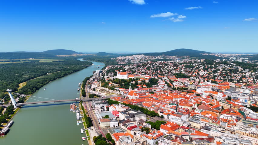Old own of Bratislava and the Danube with UFO bridge over it. Aerial perspective on the city scenery with green mountains at backdrop.