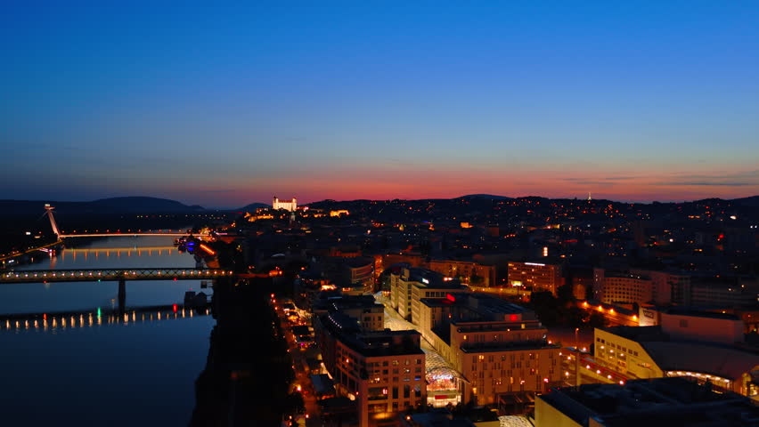Drone rising above the waterscape of the Danube. Beautiful old town of Bratislava, Slovakia at night.