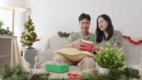 Happy young couple enjoying christmas at home, xmas tree and presents adorn festive living room, people celebrating holiday joyfully on couch, exchanging gifts, sharing love, togetherness. - Powered by Shutterstock - Get 15% off with code: PIKWIZARD15