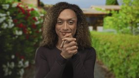Woman covers face with hands then uncovers it with a smile near building archway in green park foliage; joy. - Powered by Shutterstock - Get 15% off with code: PIKWIZARD15