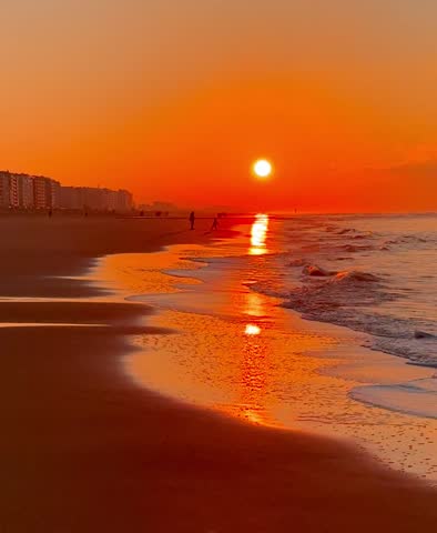 Beautiful golden sunset over the North sea, bright sun, people walking along the shore, city in the background. 