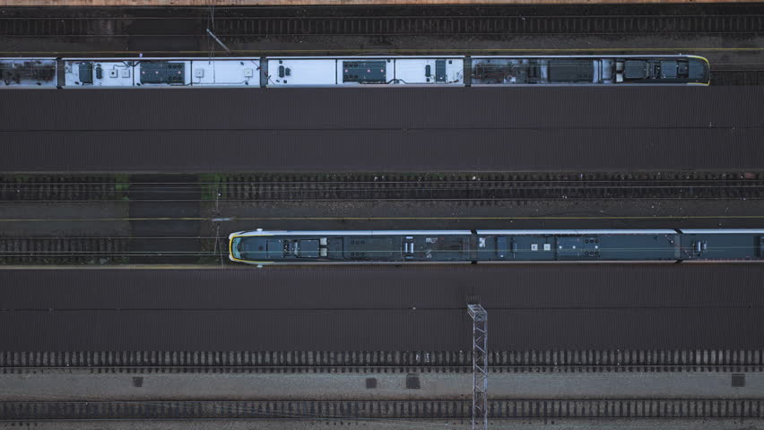 Vertical drone shot rising above passenger platforms of Zagreb Main Railway Station, with two parked passenger trains while a third train arrives, showing busy urban rail traffic.