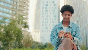A content young man with curly hair smiles while using his smartphone outdoors. He represents digital communication and modern connection, perfect for urban lifestyle, technology - Powered by Shutterstock - Get 15% off with code: PIKWIZARD15