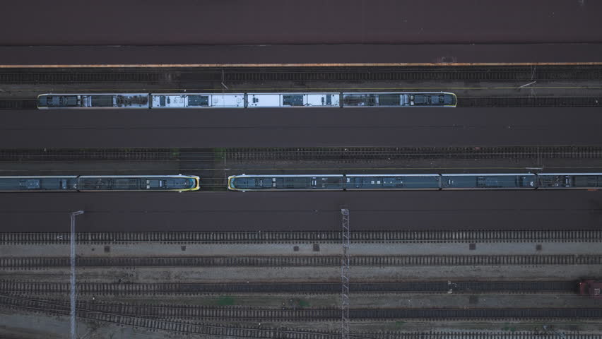 Vertical drone shot rising above passenger platforms of Zagreb Main Railway Station, with two parked passenger trains while a third train arrives, showing busy urban rail traffic.