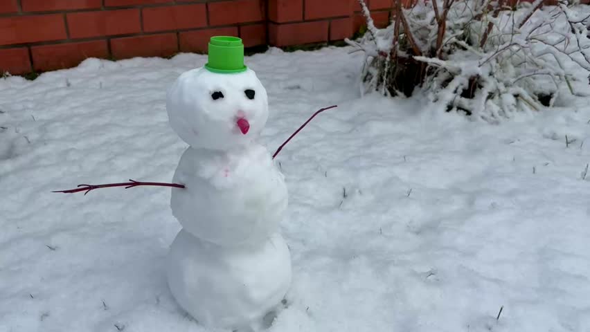 A small snowman stands in a snow-covered garden. A traditional winter activity is making a snowman from three large balls of rolled and compacted snow.