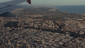 Plane-window view: red-and-white wingtip over a dense coastal city, showing shoreline and long shadows in warm low sunlight during approach. - Powered by Shutterstock - Get 15% off with code: PIKWIZARD15