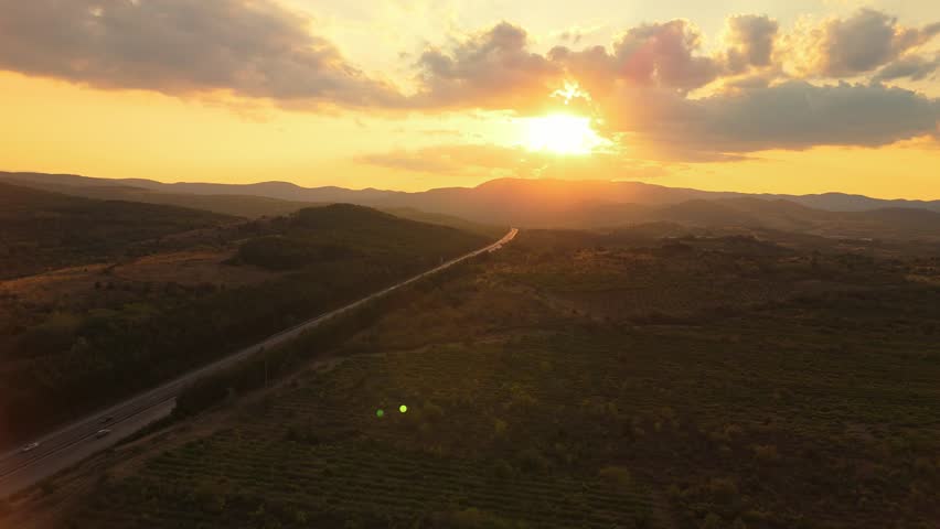 Golden hour 4K drone footage of Trakia highway near Sredna Gora mountains in Bulgaria. Cars and trucks move along the road with dramatic sunset reflections in a scenic natural setting.