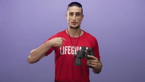 Man lifeguard in red shirt holding binoculars and points finger to chest in studio with purple backdrop; confidence duty. - Powered by Shutterstock - Get 15% off with code: PIKWIZARD15
