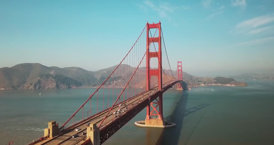 Stunning aerial shot of the Golden Gate Bridge glowing in warm sunset light over the water.