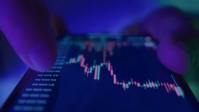 Close up of crypto trader checks investment chart on smartphone under blue and purple neon light, analyzing financial markets, stocks and cryptocurrency prices. - Powered by Shutterstock - Get 15% off with code: PIKWIZARD15