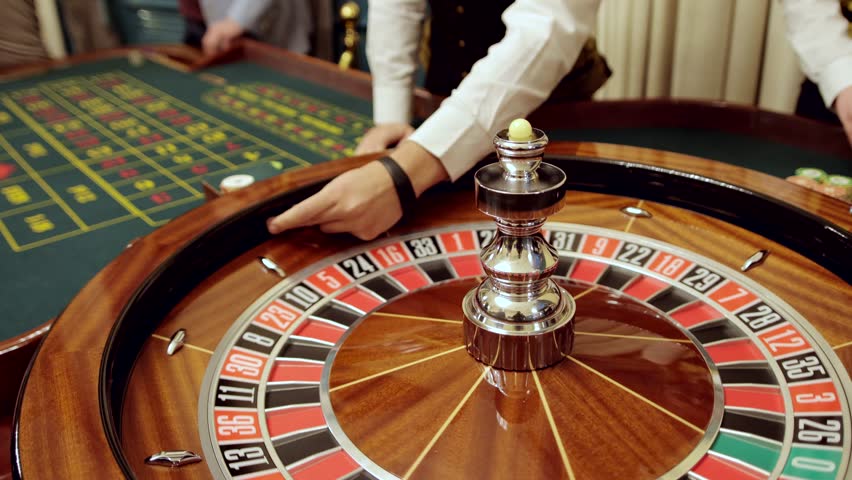 Croupier behind gambling table in a casino. Roulette wheel and croupier hand. Casino players making bets at a roulette table.