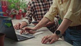 Senior woman and her younger female coworker discussing ideas and using laptop at worktable surrounded by potted plants in sunlit greenhouse - Powered by Shutterstock - Get 15% off with code: PIKWIZARD15