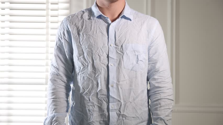 Man putting on creased shirt indoors, closeup