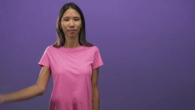 Woman covers eyes with right hand and smiles in purple studio wearing pink t shirt and brunette hair; playful surprise joy. - Powered by Shutterstock - Get 15% off with code: PIKWIZARD15