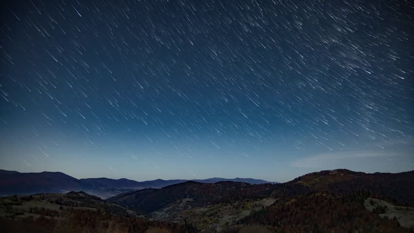 Stunning star trails time-lapse over a dark mountain landscape with forests and hills. Capturing the Earth