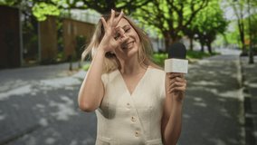 Woman reporter holding microphone makes ok sign with hand over eye on a street; playful interview moment. - Powered by Shutterstock - Get 15% off with code: PIKWIZARD15